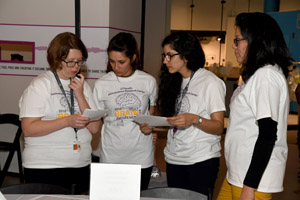 four young women dressed in white lab coats standing together and looking at index cards